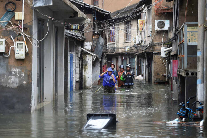 Menschen gehen zwischen Häusern auf einer von Wasser überfluteten Straße. Mit heftigem Regen und Sturmböen hat Taifun Lekima das chinesische Festland erreicht.