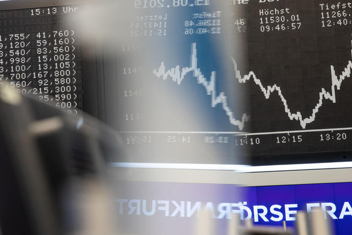 Die Dax-Kurve (r) spiegelt sich im Handelssaal der Börse in dem Firmenschild (M) von Händlern.