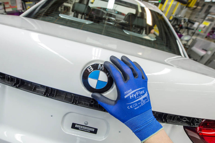 Ein Mitarbeiter montiert im BMW-Werk in Dingolfing (Bayern) ein BMW-Emblem auf den Kofferraumdeckel eines Fahrzeugs der 7er Reihe. (Archivbild)