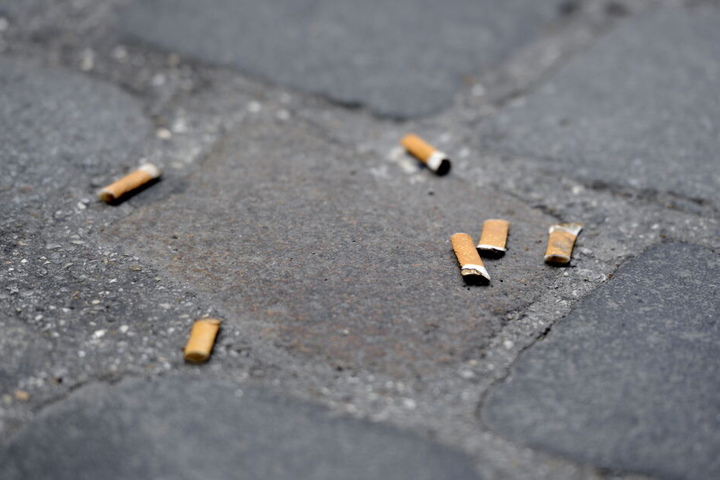 Zigarettenkippen liegen auf einem Gehweg mit Pflastersteinen