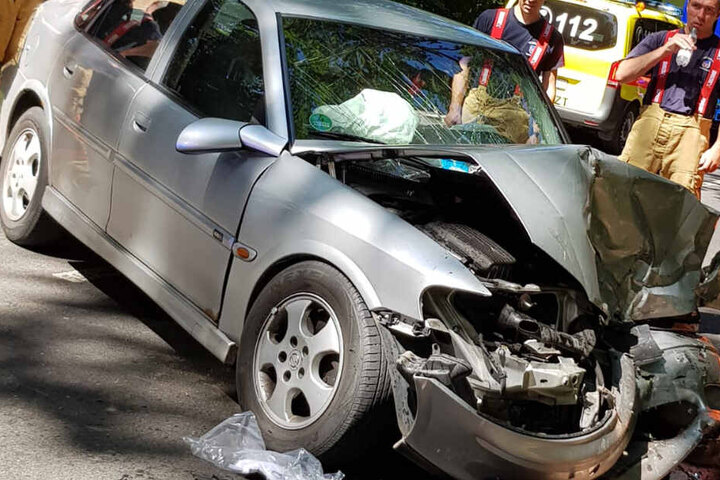 Einsatzkräfte betrachten das beschädigte Auto.