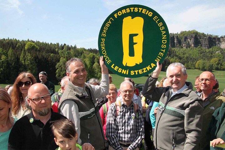 Umweltminister Thomas Schmidt und Uwe Borrmeister, Leiter des Forstbezirkes Neustadt halten stolz ein XXL-Logo vom "Forststeig Elbsandstein" in die Höhe.