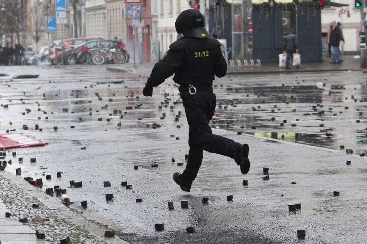 Ein Polizist rennt über eine Kreuzung der Karl-Liebknecht-Straße, die mit geworfenen Steinen übersät ist.