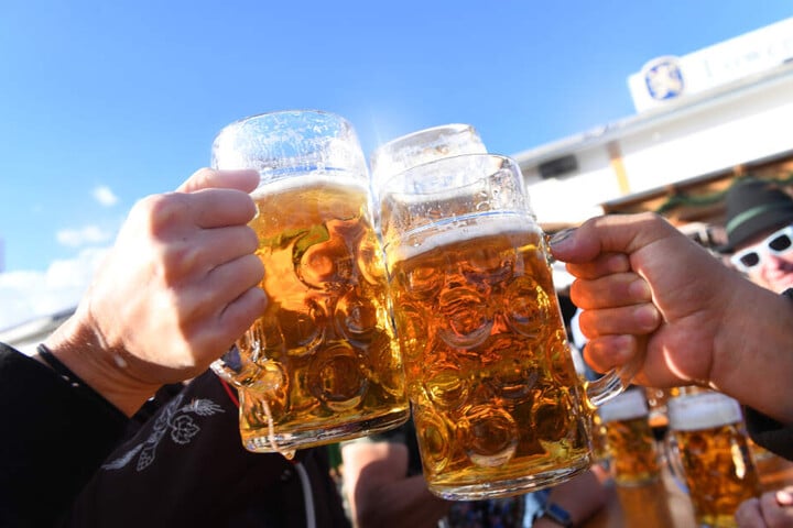 Besucher stoßen auf dem Oktoberfest mit Maßkrügen voller Bier an.