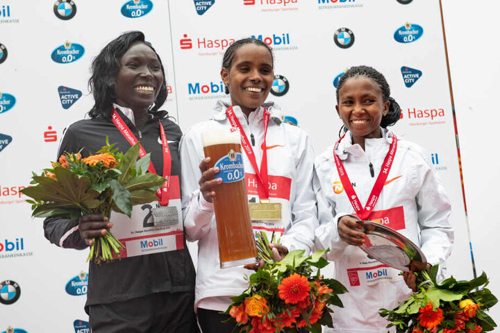 Marathon-Siegerin Dibabe Kuma (Mitte) aus Äthiopien, die zweitplatzierte Magdalyne Masai (l) aus Kenia und die drittplatzierte Failuna Matanga aus Tansania jubeln beim 34. Hamburg Marathon bei der Siegerehrung.