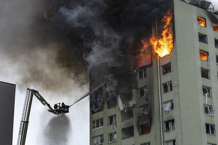 Feuerwehrleute löschen auf einer Drehleiter einen Brand in einem 12-stöckigen Mehrfamilienhaus, das durch eine Gasexplosion schwer beschädigt wurde.