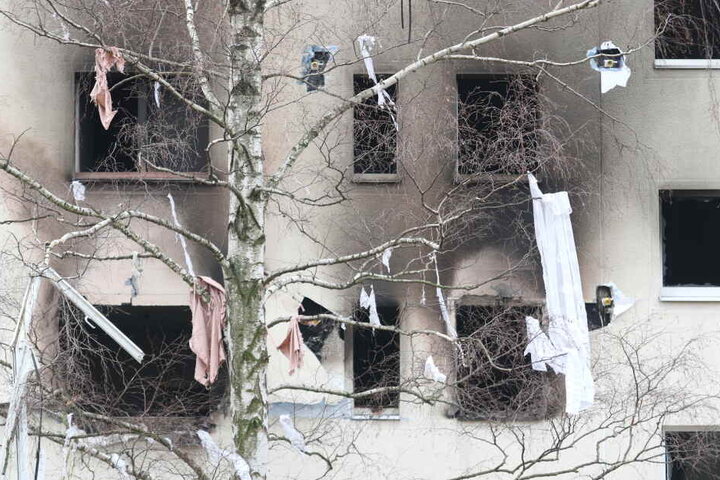 Eine Birke gegenüber des Plattenbaus hängt nach der Explosion voller Kleidungsstücke. Auch ein Fensterrahmen ist unten links zu erkennen.