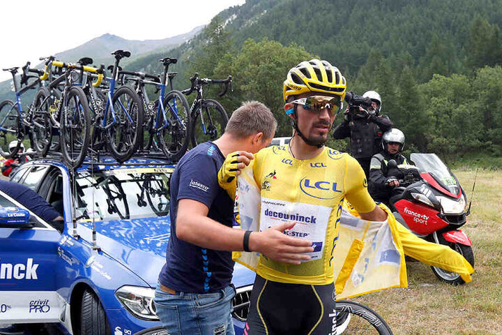 Julian Alaphilippe aus Frankreich vom Team Deceuninck-Quick-Step im gelben Trikot zieht sich vor dem Teamwagen eine Jacke an