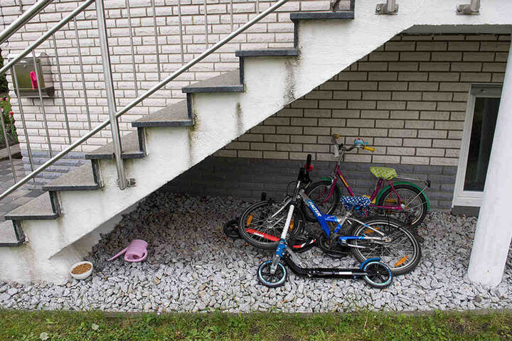 Kinderfahrräder und ein Tretroller liegen unter der Treppe des Hauses.