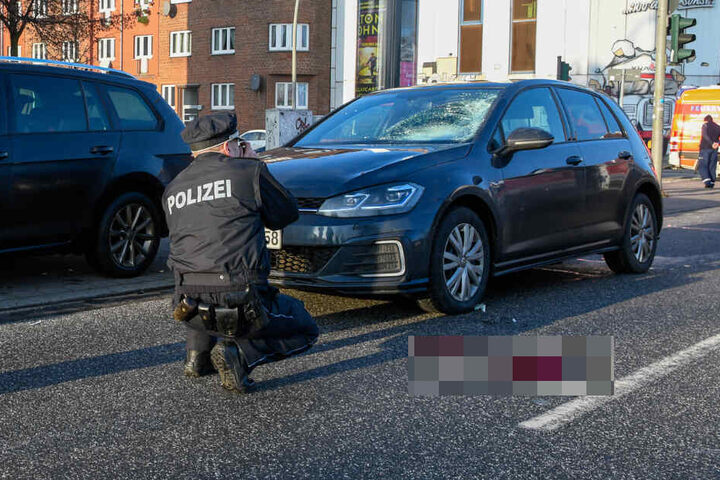 Ein Polizist fotografiert das Unfallauto. Auf der Straße ist eine große Blutlache zu sehen.