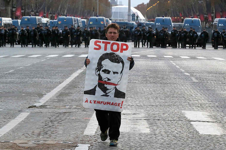 Der Demonstrant trägt ein Plakat mit dem Abbild des französischen Präsidenten auf der Champs Elysees, im Hintergrund stehen Polizisten. Frankreichs Regierung fürchtet weitere Ausschreitungen in Paris und will mit einem massiven Aufgebot von Sicherheitskrä