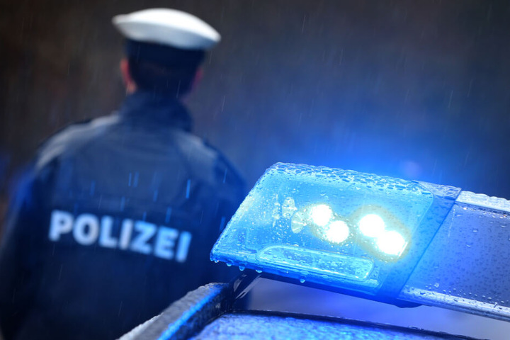 Ein Polizist steht im Regen neben seinem Polizeifahrzeug. (Symbolbild)