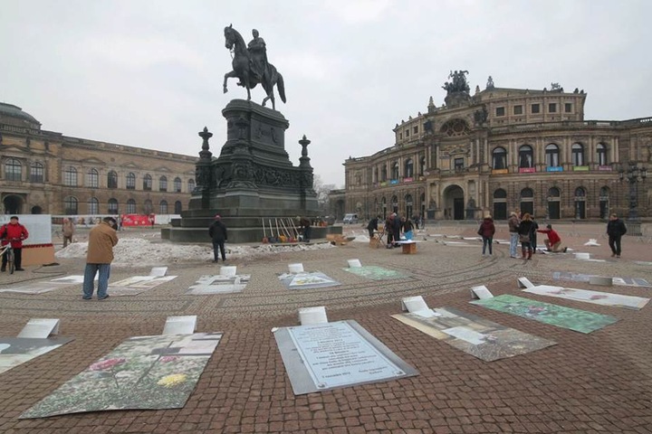 Auf dem Theaterplatz liegen Fotos von Gräbern von Flüchtlingen, die im Mittelmeer ertrunken sind.