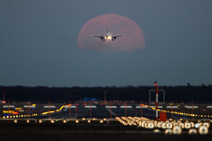 Frankfurt am Main: Ein Passagierflugzeug befindet sich am Frankfurter Flughafen im Landeanflug, während im Hintergrund der Vollmond aufgeht.