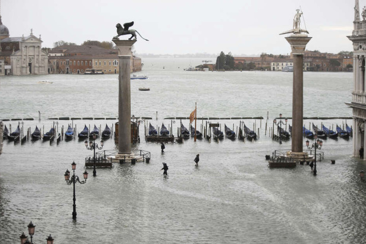 Menschen gehen knietief in Wasser über den überfluteten Markusplatz.