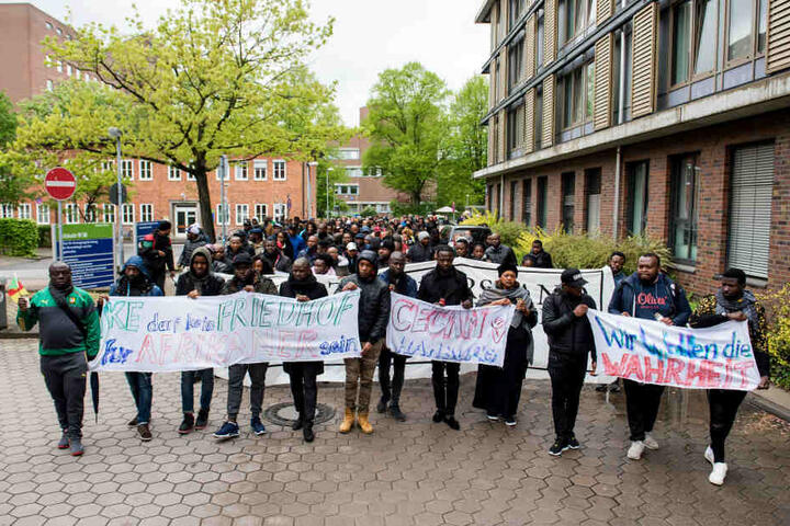 Teilnehmer eines Trauermarsches gehen über das Gelände des Universitätskrankenhauses Hamburg-Eppendorf (UKE) und halten ein Transparent mit der Aufschrift "UKE darf kein Friedhof für Afrikaner sein".