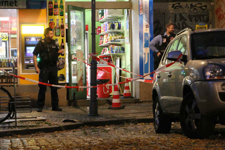 Polizisten mit Maschinenpistolen sichern den Tatort in der Neuköllner Herrfurthstraße ab. Liegen unter den drei rot-weißen Verkehrshütchen die Patronenhülsen?