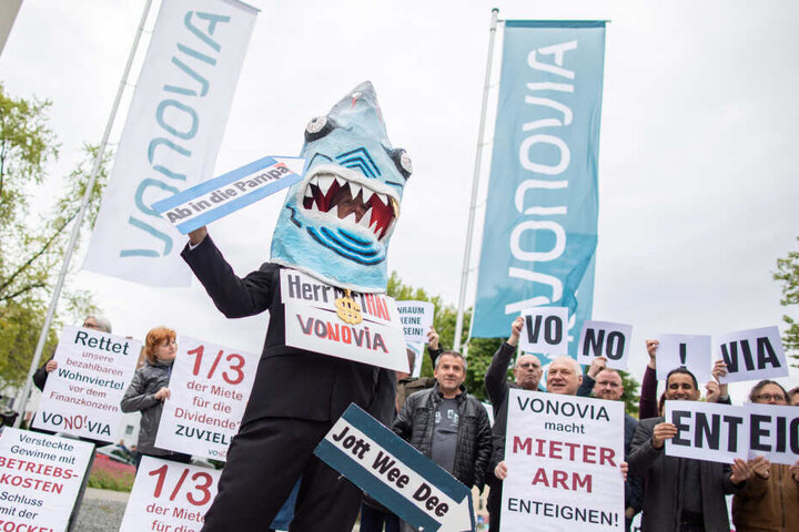 Ein Demonstrant in einem Hai-Kostüm mit einem Schild um den Hals "Herr Miethai Vonovia" steht vor der Vonovia Hauptversammlung vor dem Ruhrcongress.