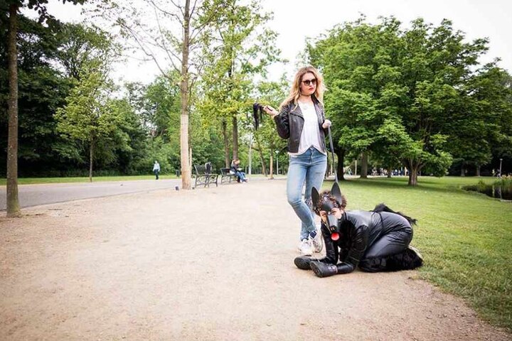 Ines führt Leila im Fetish-Hundekostüm durch den Park.