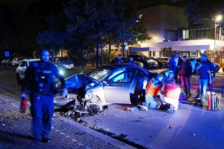 Rettungskräfte kümmern sich um den neben dem Auto liegenden Unfallfahrer.