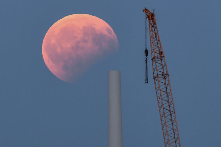 Blick auf die partielle Mondfinsternis über einer Baustelle für eine Windenergieanlage im brandenburgischen Sieversdorf.