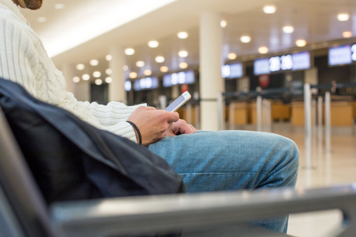 Ein Mann vertreibt sich die Wartezeit am Flughafen mit seinem Smartphone. (Symbolbild)