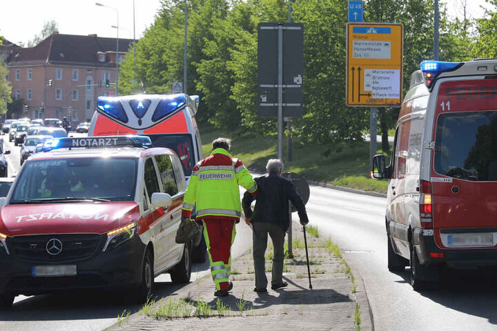 Ein Beamter der Feuerwehr muss den Unfallfahrer, einen 82-jährgen Senior, der am Stock geht, nach dem Unfall stützen.