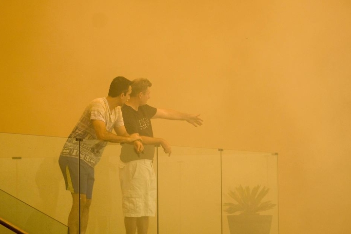 Einwohner stehen vor einem Haus im rötlichen Rauch eines Buschfeuers.