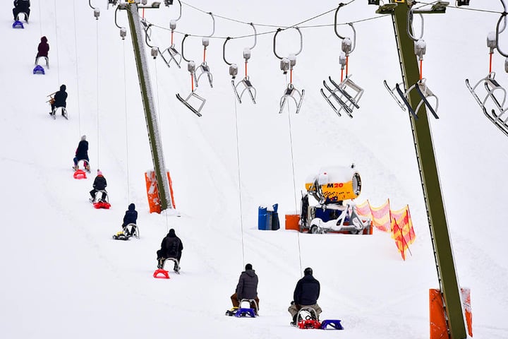 Besucher lassen sich eine Piste mit Schlitten von einem Lift hochziehen