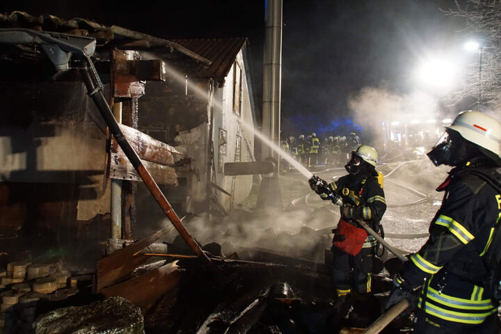 Zwei Feuerwehrkräfte löschen das Gebäude neben einer Sammelunterkunft.