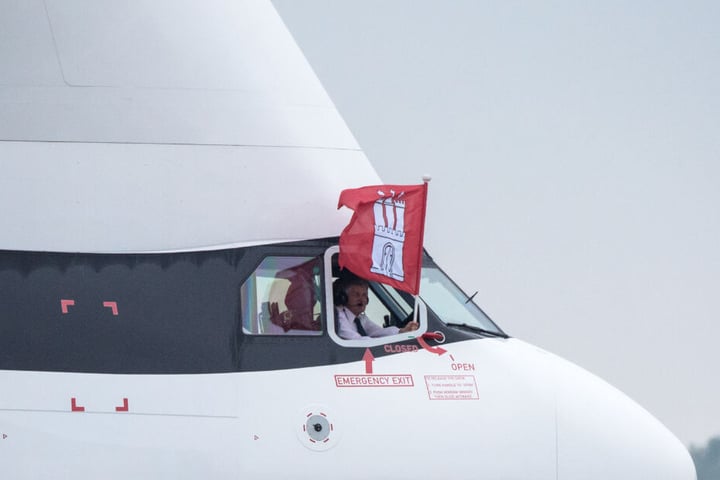 Der Airbus-Pilot hält nach der ersten Landung des "BelugaXL" in Hamburg eine Fahne der Stadt aus dem Cockpit-Fenster.