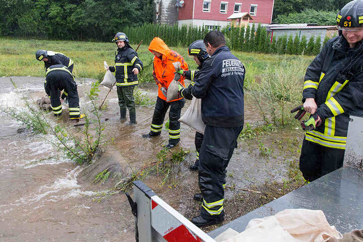 Feuerwehrleute schichten im Suhler Stadtteil Neundorf Sandsäcke auf.