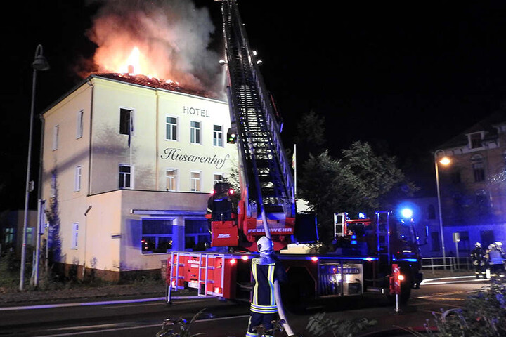 Flammen schießen aus dem Dach des Hotels „Husarenhof“, Feuerwehrleute löschen
von der Drehleiter aus.