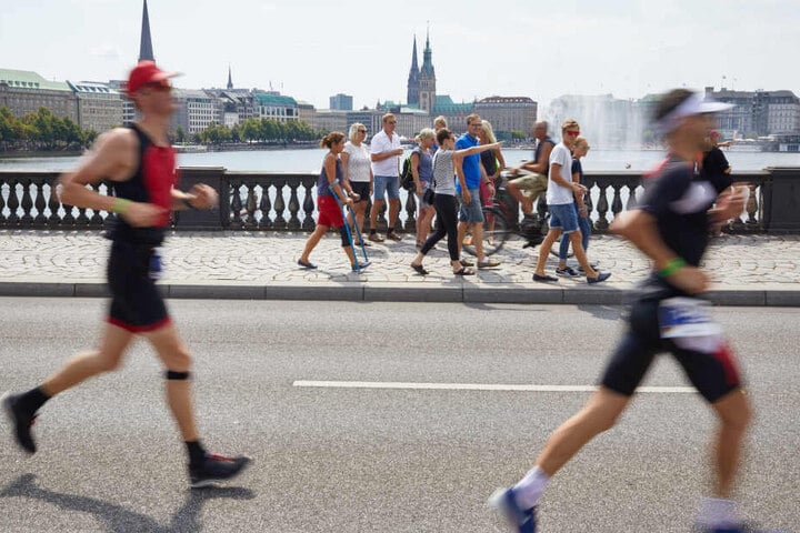 Triathleten laufen über die Lombardsbrücke. Im Hintergrund sind die Binnenalster und das Rathaus zu sehen.