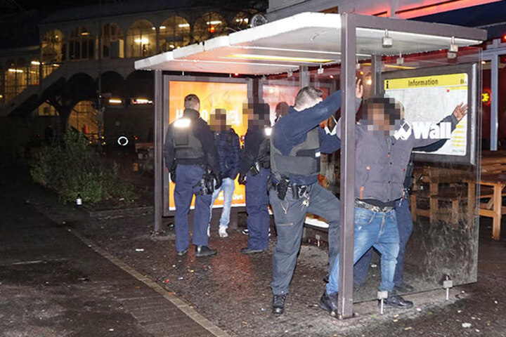 An einer angrenzenden Bushaltestelle kontrollieren Beamte eine involvierte Personengruppe.