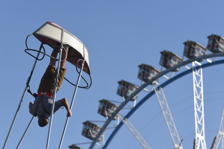 Ein Wiesnbesucher überschlägt sich in einer Schiffschaukel auf dem Oktoberfest vor dem Riesenrad.