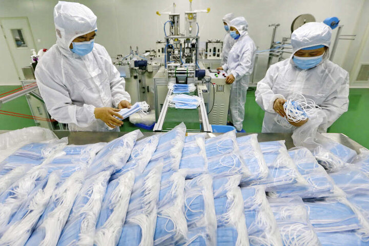 Arbeiter in einer Fabrik packen Schutzmasken ein.
