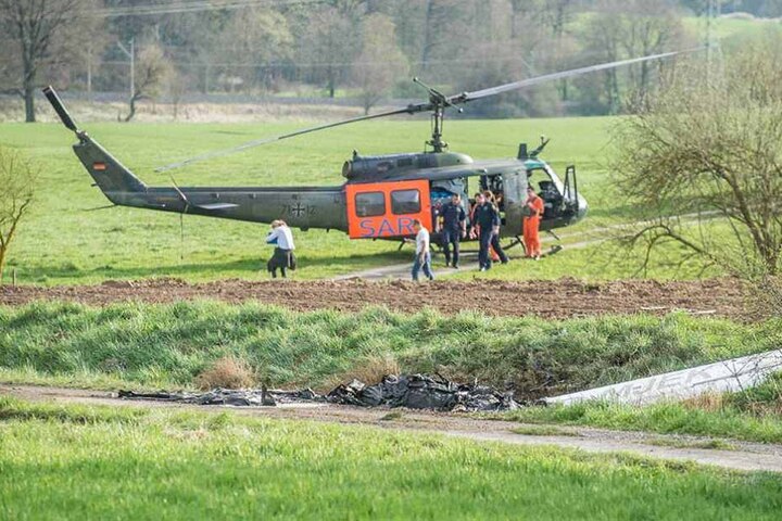 ie Überreste eines abgestürzten und ausgebrannten Ultraleichtflugzeuges sind an einem Feldweg vor einem Rettungshubschrauber zu sehen.