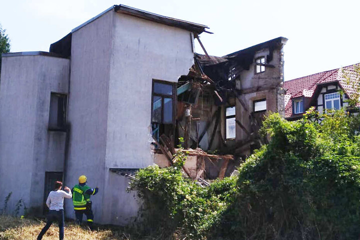 Experten betrachten das eingestürzte Wohnhaus von hinten. Hier läuft auch eine Bahnstrecke entlang.