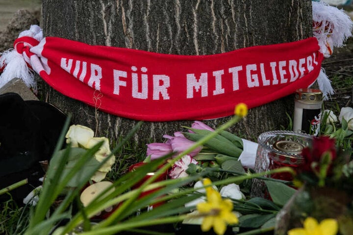 Blumen und Kerzen sowie ein Fan-Schal vom 1. FC Union haben Menschen auf einem Parkplatz an der Stahlheimer Straße abgelegt.