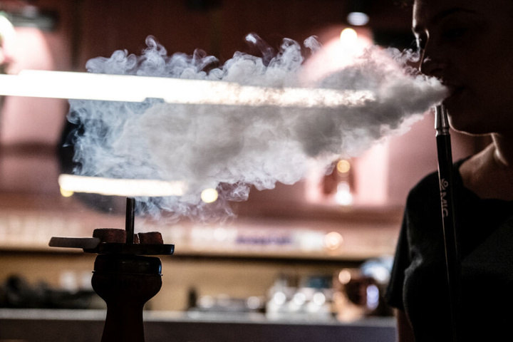 Eine Frau stößt nach einem Zug an der Shisha-Pfeife den Qualm aus.