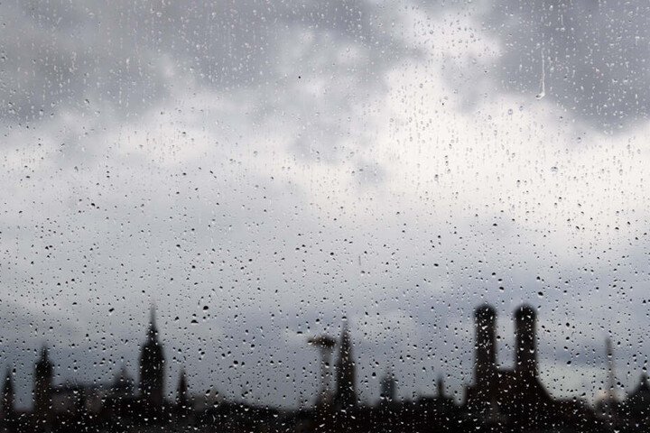 Die Skyline von München ist hinter Tropfen auf einer Fensterscheibe zu sehen.