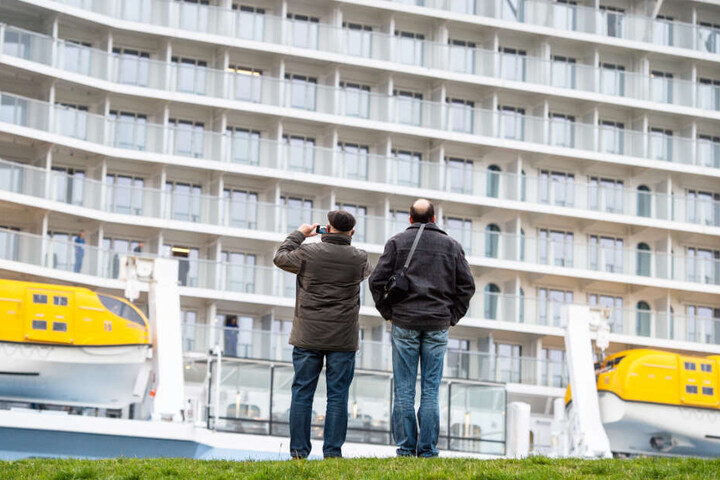 Schaulustige stehen auf einem Deich und beobachten, wie das Kreuzfahrtschiff "Spectrum of the Seas" während der Überführung auf der Ems von Schleppern durch die Dockschleuse manövriert wird.