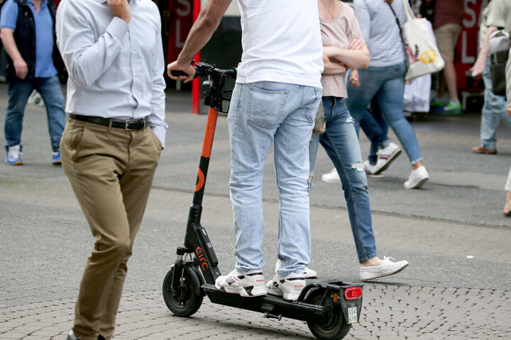 Mit einem Elektro Tretroller fährt ein Mann durch die Fußgängerzone.