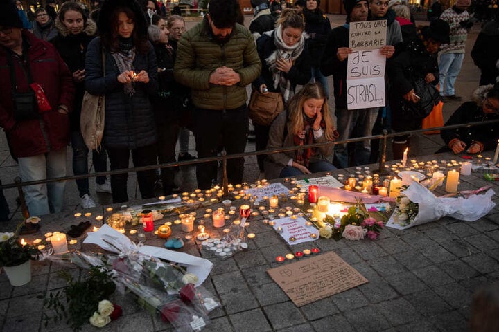 Trauernde stehen nahe dem Straßburger Weihnachtsmarkt hinter zahlreichen brennenden Kerzen.