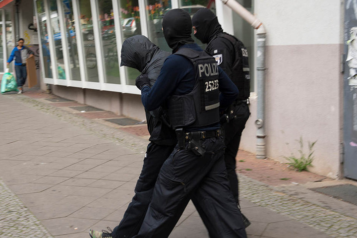 Polizeibeamte führen einen der Verdächtigen mit Handschellen ab.