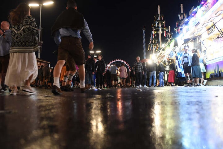 Die Lichter der Wiesn spiegeln sich auf dem nassen Straße auf der Theresienwiese. Am zweiten Wochenende kann es in München regnen.