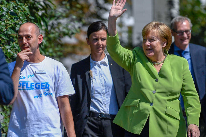 Bundeskanzlerin Angela Merkel winkt neben Pfleger Ferdi Cebi.