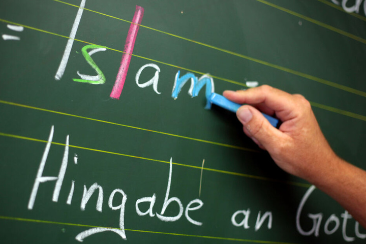Ein Religionslehrer schreibt an einer Schule während des islamischen Religionsunterrichts an der Tafel. (Archivbild)
