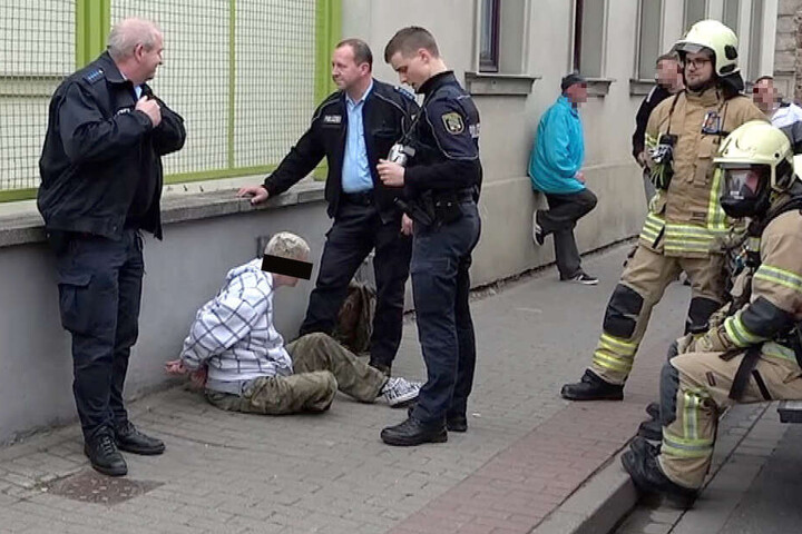 Die Tatverdächtige sitzt in Handschellen auf dem Boden vor dem Mietshaus, in dem sie gezündelt haben soll.